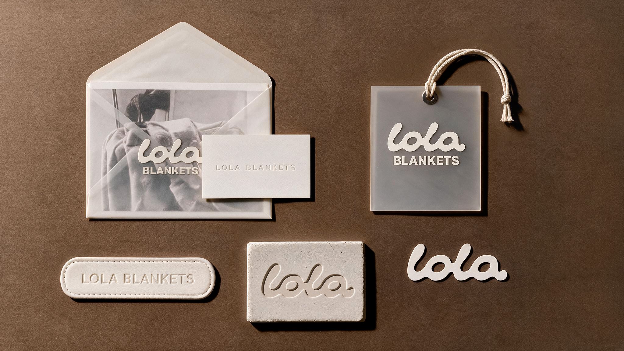 Brand collateral rendering for Lola Blankets featuring a vellum envelope, business card, hangtag, woven label and embossed patches on a brown backdrop by TRUFFL branding agency.