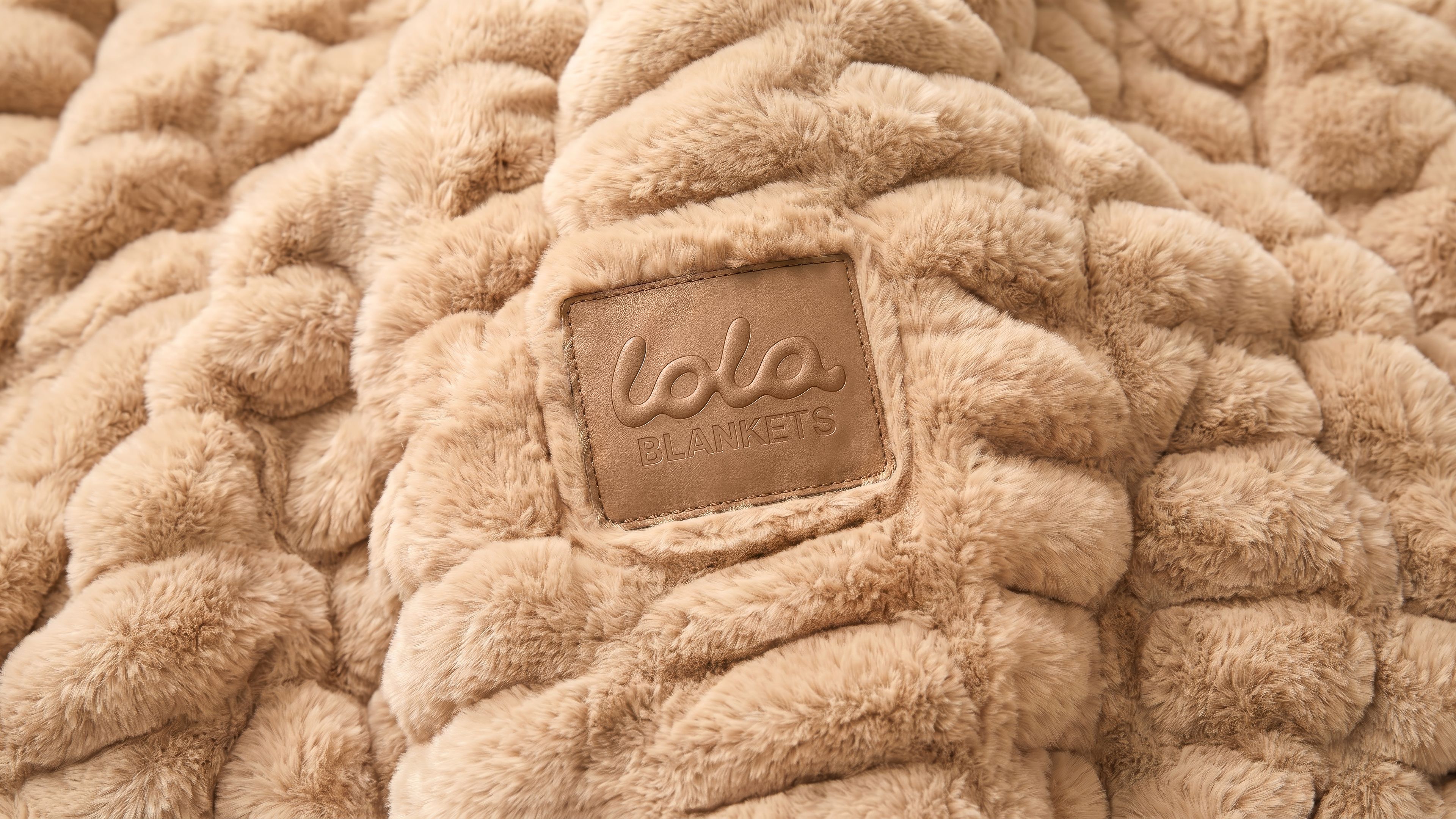 Product detail rendering for Lola Blankets featuring the embossed leather Lola Blankets patch on a camel ribbed faux fur blanket by TRUFFL branding agency.