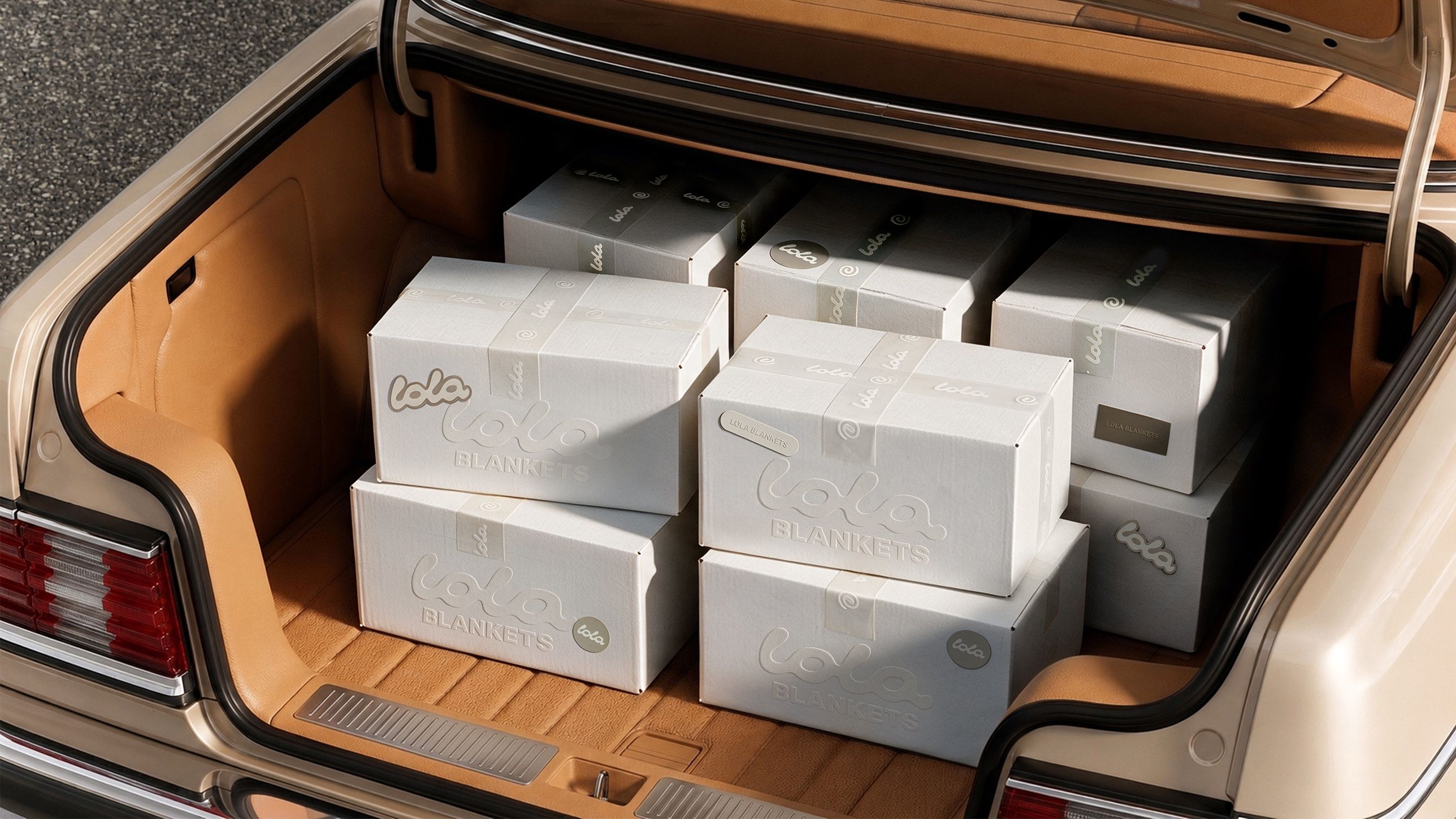 Packaging rendering for Lola Blankets featuring embossed shipping boxes with logo stickers and branded tape loaded in a vintage car trunk by TRUFFL branding agency.